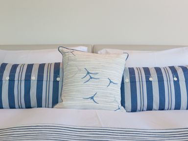 A bed with white and blue striped pillows and a white pillow with blue leaf patterns at Crystal Bay in St Ives