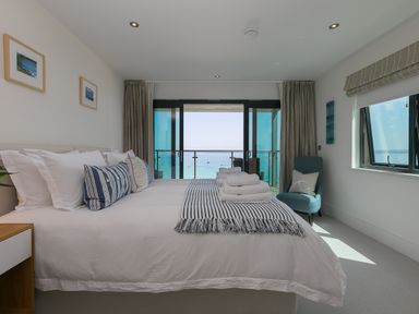 A bedroom with a large bed towels on bed a chair and a balcony overlooking the sea at Crystal Bay in St Ives