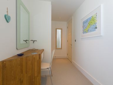 A narrow hallway with a wooden desk and chair a mirror on the wall and a framed map at Crystal Bay in St Ives