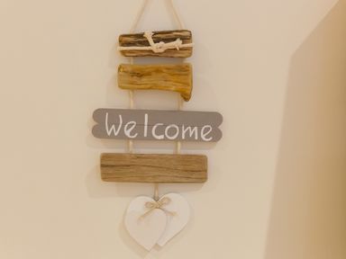 A wooden welcome sign with two white hearts hanging on a beige wall at Crystal Bay in St Ives