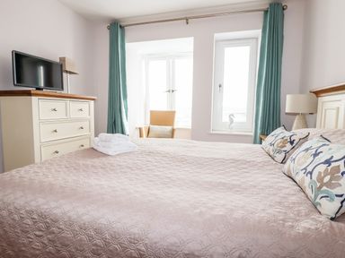 A bedroom with a bed a dresser with a television green curtains and a chair at 16 Ocean Heights in Newquay