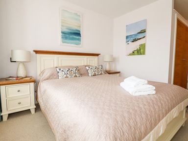 A bedroom with a bed with pillows and folded towels bedside tables with lamps and wall art at 16 Ocean Heights in Newquay