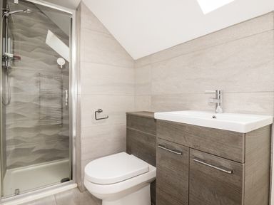 A bathroom with a shower enclosure a toilet and a sink with wooden cabinetry at 16 Ocean Heights in Newquay