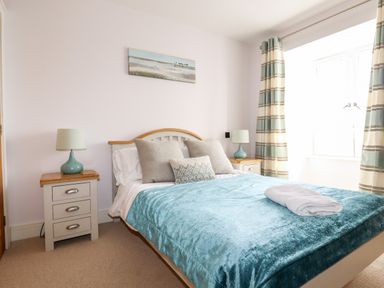 A bedroom with a bed two bedside tables lamps and a window with curtains at 16 Ocean Heights in Newquay