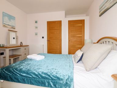 A bedroom with a bed covered in a blue blanket two wooden doors and a vanity table with a mirror at 16 Ocean Heights in Newquay