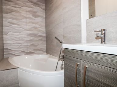 A bathroom with a white bathtub a hand shower and a sink with a textured cabinet at 16 Ocean Heights in Newquay