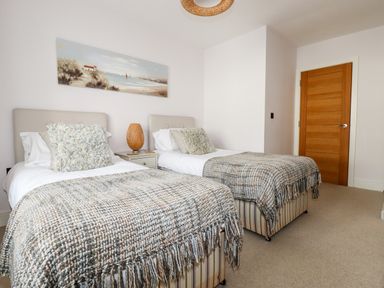 A bedroom with two single beds a nightstand with a wicker lamp and a wooden door at 16 Ocean Heights in Newquay