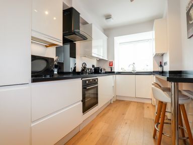 A kitchen with white cabinets black countertops and wooden floor at 16 Ocean Heights in Newquay