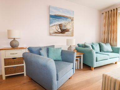 A room with two blue sofas a side table with baskets and lamps and a painting of a boat on the wall at 16 Ocean Heights in Newquay