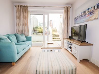 A living room with a blue sofa table and striped ottoman in front of a sliding glass door at 16 Ocean Heights in Newquay
