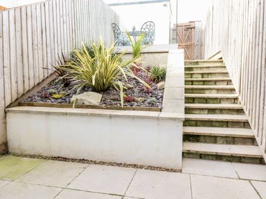An outdoor area with a raised garden bed, plants, concrete steps, and a wooden fence at 16 Ocean Heights in Newquay