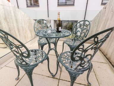 An outdoor patio with a metal table and four chairs and a bottle with a glass on the table at 16 Ocean Heights in Newquay