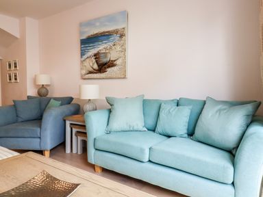 A living room with two sofas a wooden coffee table two lamps and a painting of a boat on a beach at 16 Ocean Heights in Newquay