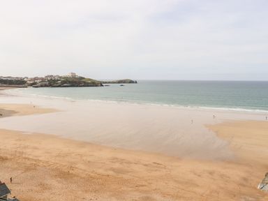 A wide sandy beach with a few people walking near the water and a headland with buildings in the distance at 16 Ocean Heights in Newquay