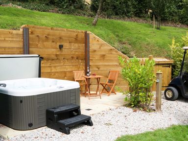 An outdoor area with a hot tub wooden table and chairs plants and a golf cart at Little Silver Pheasant in High Bickington