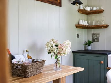 A kitchen corner with a wooden table holding a basket with bottles and a vase with flowers at Little Silver Pheasant in High Bickington