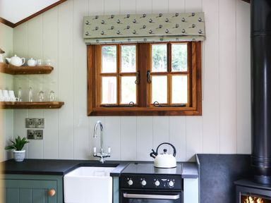 A kitchen with a window above a sink and stove with a kettle and a wood burning stove at Little Silver Pheasant in High Bickington