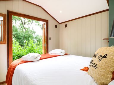 A bedroom with a bed, white bedding, an orange throw, pillows, and an open door showing green trees at Little Silver Pheasant in High Bickington