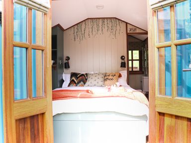 A bedroom with a bed with cushions and a blanket between open wooden doors at Little Silver Pheasant in High Bickington