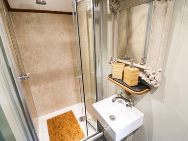 A bathroom with a shower enclosure a small sink a decorative mirror and wooden soap dispensers at Little Silver Pheasant in High Bickington