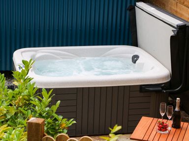 A hot tub with bubbling water next to a wooden table with strawberries and champagne at Little Silver Pheasant in High Bickington