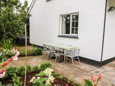 A patio with a table and six metal chairs next to a white house with a window surrounded by plants and flowers at Teach Chiuin in Coolaheen near Cappoquin County Waterford