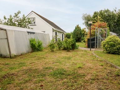 A garden area with grass and shrubs next to a white house and a greenhouse at Teach Chiuin Coolaheen near Cappoquin County Waterford