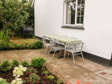 An outdoor patio area with a green table and metal chairs next to a white building with a window at Teach Chiuin in Coolaheen near Cappoquin County Waterford
