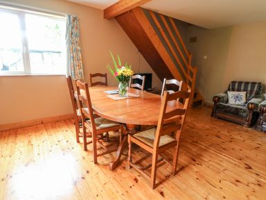 A dining area with a wooden table and six chairs next to a window and wooden stairs in a living space at Teach Chiuin in Coolaheen near Cappoquin County Waterford