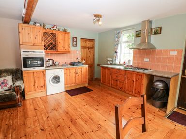 A kitchen with wooden cabinets appliances a washing machine a gas stove a trash bin and a wooden floor at Teach Chiuin in Coolaheen near Cappoquin County Waterford