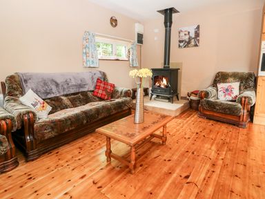 A living room with a wooden floor a sofa an armchair a coffee table with flowers and a wood burning stove at Teach Chiuin in Coolaheen near Cappoquin County Waterford