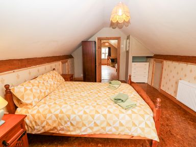 A bedroom with a double bed covered in a patterned bedspread with folded towels on top a wooden nightstand a lamp a wardrobe and a chest of drawers at Teach Chiuin in Coolaheen near Cappoquin County Waterford