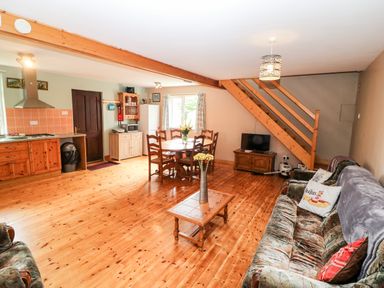 An open living room and kitchen with wooden floors a dining table chairs a wooden coffee table a sofa and a television under wooden stairs at Teach Chiuin Coolaheen near Cappoquin County Waterford