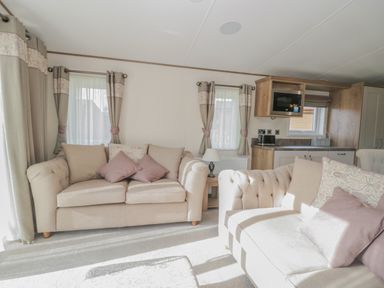A living room with two beige sofas with cushions a small wooden side table with a lamp and a kitchen area with cupboards a microwave and a toaster at 22 Sherwood South Lakeland Leisure Village near Warton