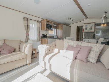 A living room with beige sofas and pink cushions next to a kitchen area at 22 Sherwood South Lakeland Leisure Village near Warton