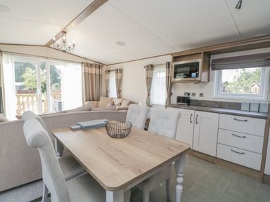 A dining area with a wooden table and chairs next to a kitchen with white cabinets and a microwave at 22 Sherwood South Lakeland Leisure Village near Warton