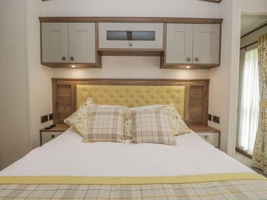 A bedroom with a bed featuring a yellow tufted headboard and overhead cabinets at 22 Sherwood South Lakeland Leisure Village near Warton