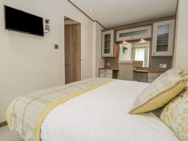A bedroom with a bed a wall-mounted TV a wooden desk with cabinets and a chair at 22 Sherwood South Lakeland Leisure Village near Warton