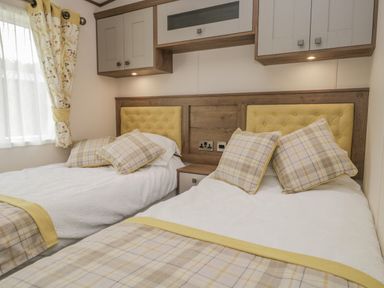 A bedroom with two single beds each with yellow headboards plaid pillows and blankets under wall cabinets at 22 Sherwood South Lakeland Leisure Village near Warton