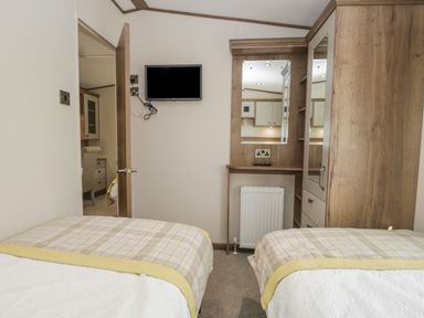 A bedroom with two single beds a wall-mounted television and a wooden wardrobe at 22 Sherwood South Lakeland Leisure Village near Warton