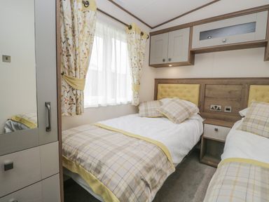 A bedroom with two single beds a window with floral curtains and built in cabinets at 22 Sherwood South Lakeland Leisure Village near Warton