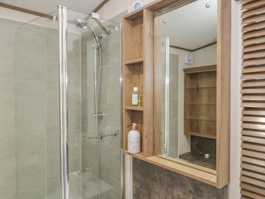 A shower area with glass door and wooden shelving with toiletries at 22 Sherwood South Lakeland Leisure Village near Warton