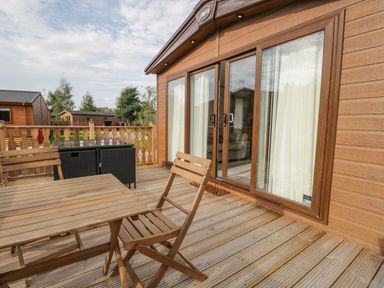 A wooden deck with a table and chairs outside a cabin with glass sliding doors at 22 Sherwood South Lakeland Leisure Village near Warton