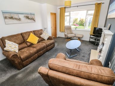 A living room with brown sofas yellow curtains a gray armchair and a blue round coffee table at 53 St Brides View in Roch