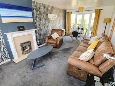 A living room with brown sofas a coffee table fireplace dining table and chairs with yellow curtains at 53 St Brides View in Roch