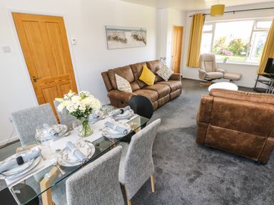 A living room with brown sofas a glass dining table set for six and a large window with yellow curtains at 53 St Brides View in Roch