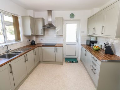 A kitchen with wooden countertops cabinets a sink a kettle a stove a microwave a knife block and a fruit bowl at 53 St Brides View in Roch