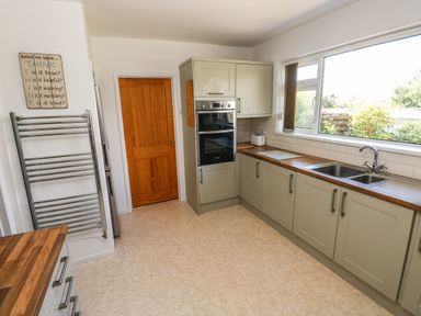 A kitchen with wooden countertops, grey cabinets, a double oven, a double sink under a large window, a wooden door, a wall-mounted towel rack, and a sign on the wall at 53 St Brides View in Roch