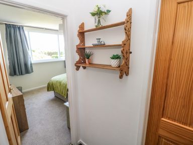 A hallway with a wooden decorative wall shelf holding plants and a small vase and an adjoining bedroom with green bedding at 53 St Brides View in Roch
