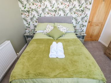 A bedroom with a double bed green bedding and three rolled white towels on the bed at 53 St Brides View in Roch
